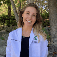 A woman in a doctor's white coat smiles at the camera.