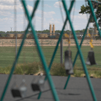 Fracking infrastructure is pictured through playground equipment at the Bella Romero Academy in Greeley on June 24, 2020. (Andy Bosselman for Colorado Newsline)